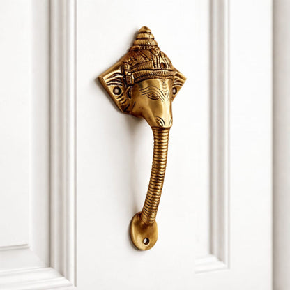 Decorative brass door handle shaped like a elephant head on a white door.