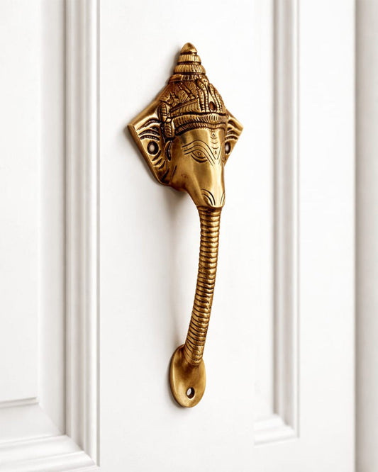 Decorative brass door handle shaped like a elephant head on a white door.