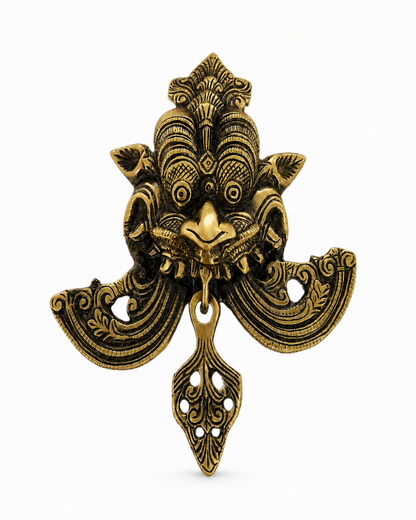 An ornate antique brass or bronze metal pendant depicting a stylized face with intricate filigree details, photographed against a clean white background.