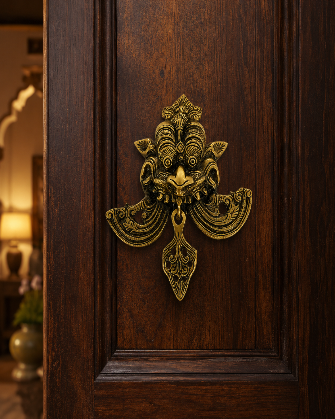 An ornate antique-style bronze door knocker mounted on a dark brown wooden door, with a softly blurred interior room visible in the background.