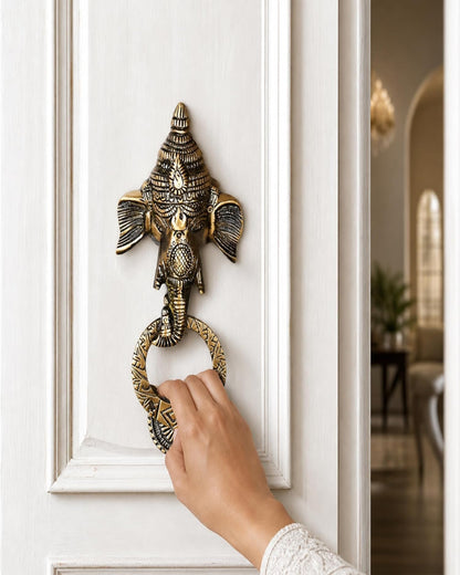 Decorative brass door knocker shaped like an elephant on a white door.