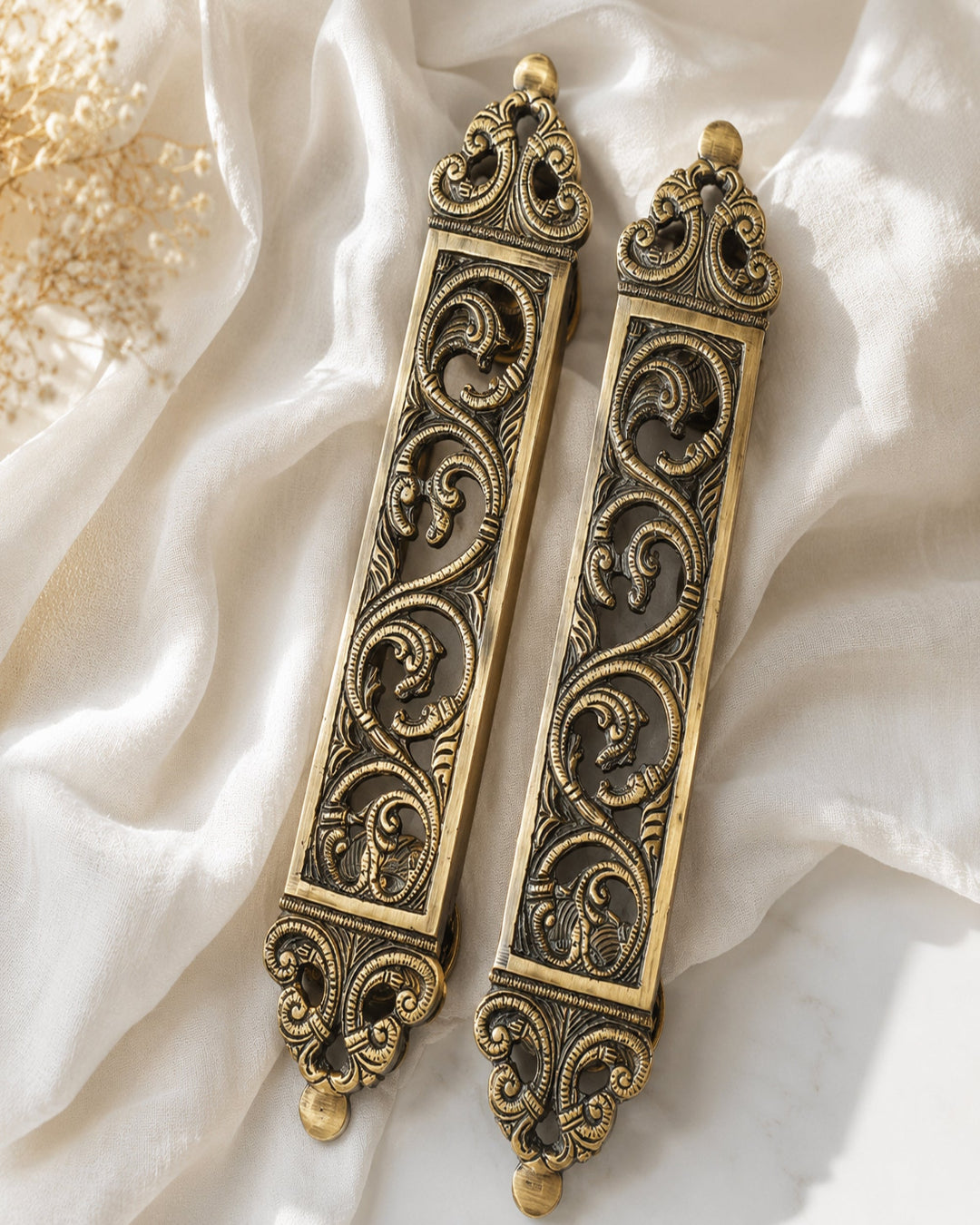 Pair of brass door pull handles on a soft white fabric background