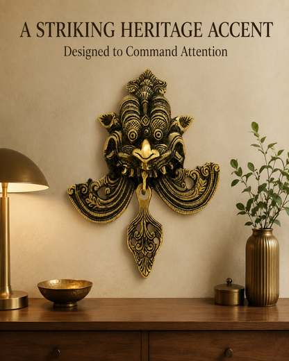 An ornate gold and black decorative wall piece mounted above a wooden console table, styled with a lit brass table lamp on the left and a potted green plant in a ribbed vase on the right. Text at the top reads 'A STRIKING HERITAGE ACCENT' and 'Designed to Command Attention'.