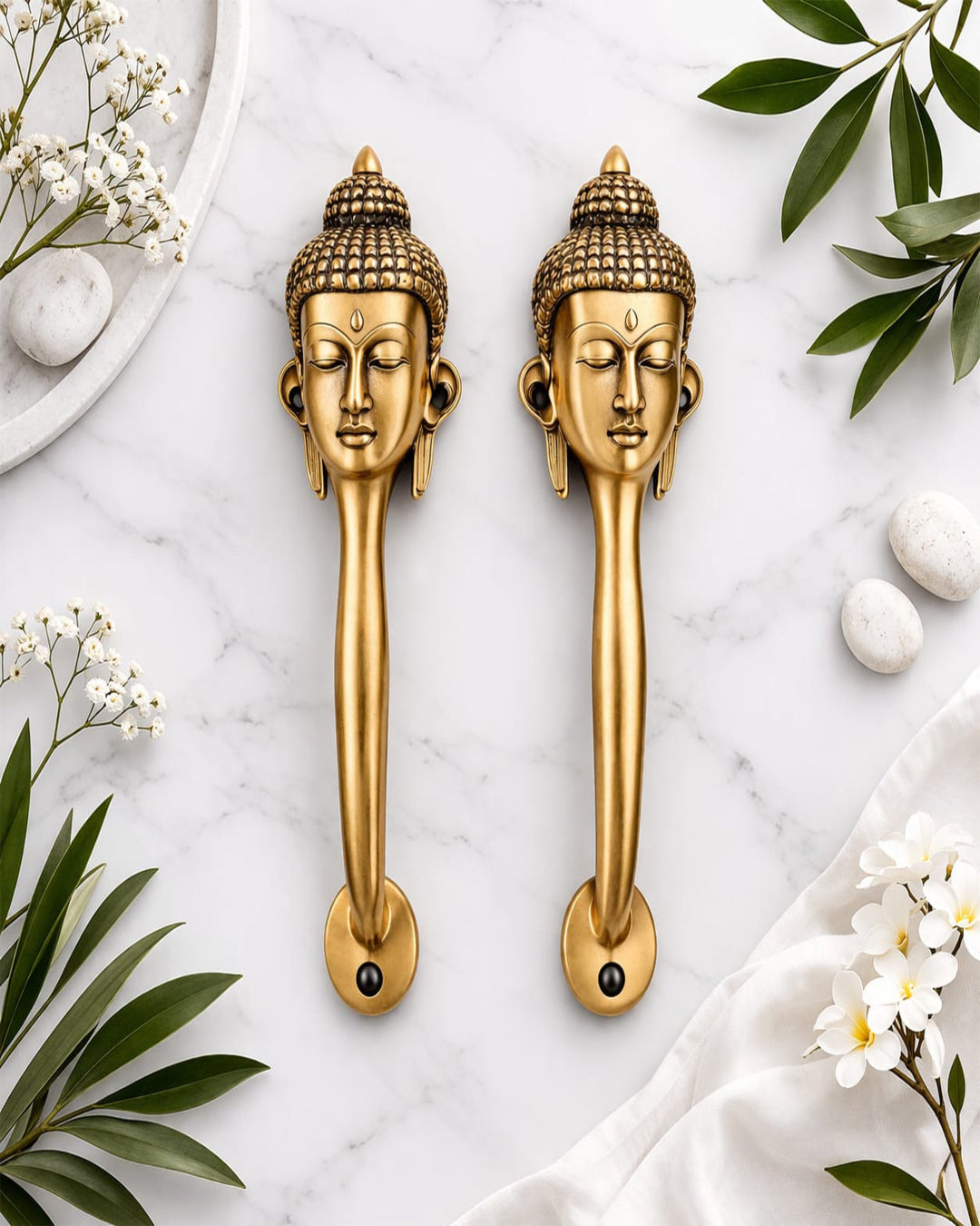 Two gold Buddha head door handles on a marble surface with decorative elements.