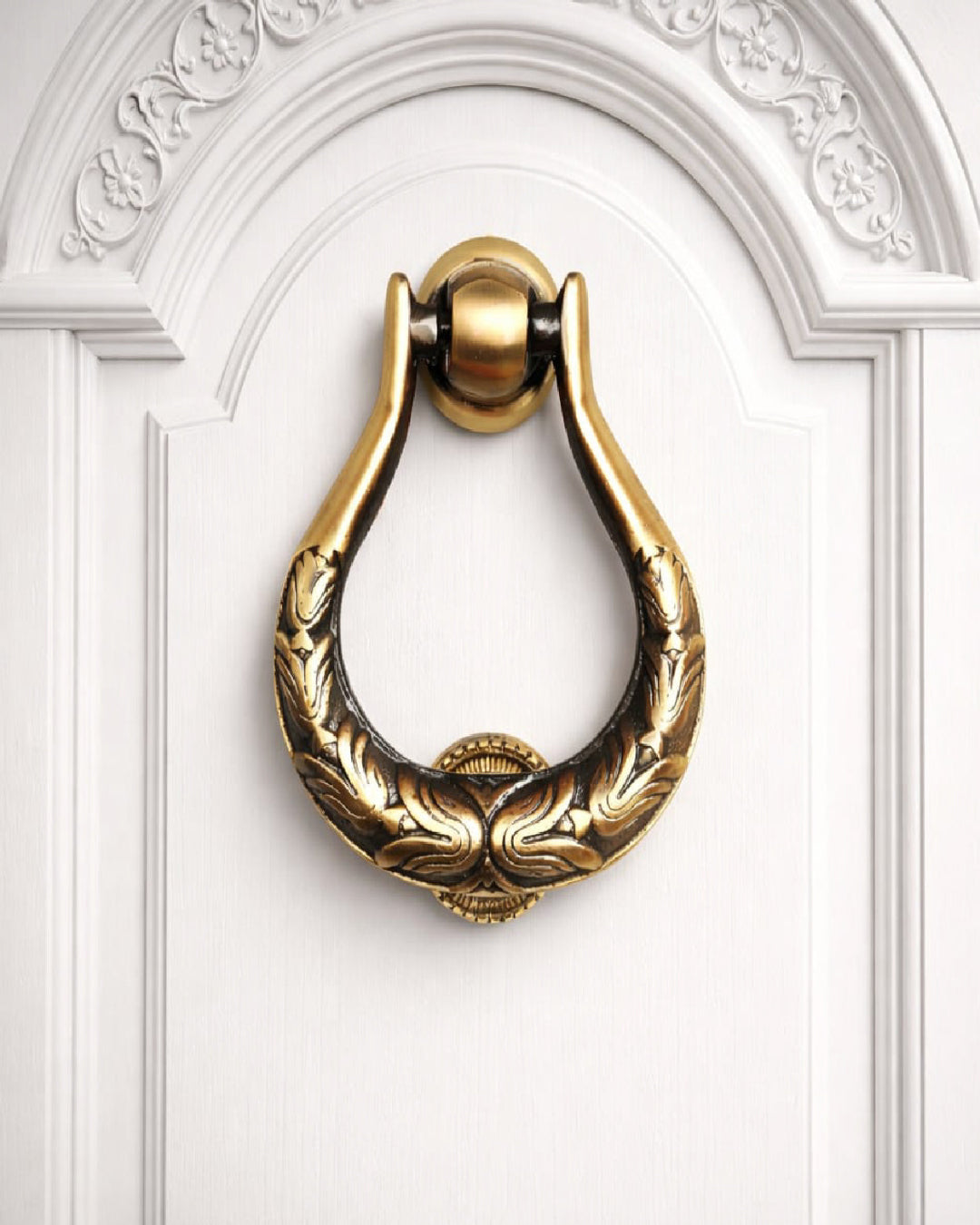 Decorative gold door knocker on a white door with intricate carvings.