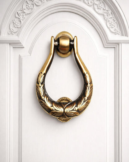 Decorative gold door knocker on a white door with intricate carvings.
