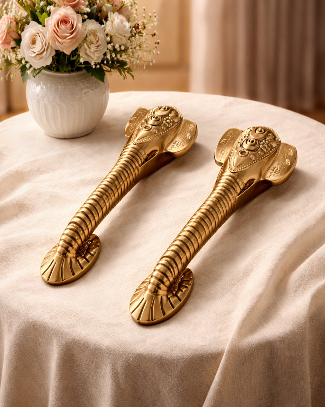 Two ornate gold door handles on a beige surface with a vase of flowers in the background.