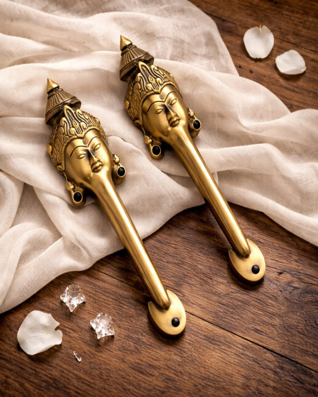 Decorative gold door handles with face designs on a wooden surface with white fabric.
