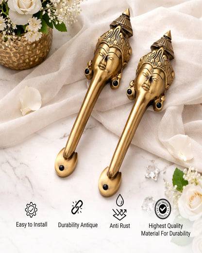 Two brass handles with decorative faces on a white fabric background with flowers.
