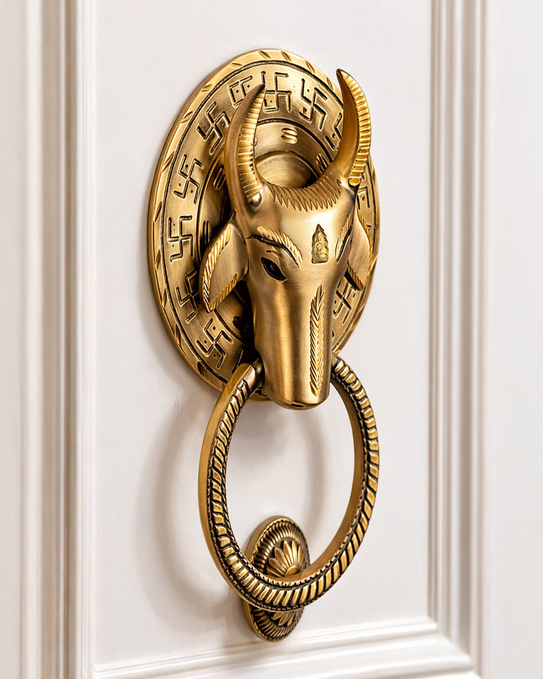 Decorative gold door knocker with bull head design on a white paneled door