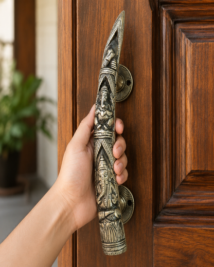 A hand holding a large, ornate bronze Ganesha door pull handle against a dark brown wooden door.