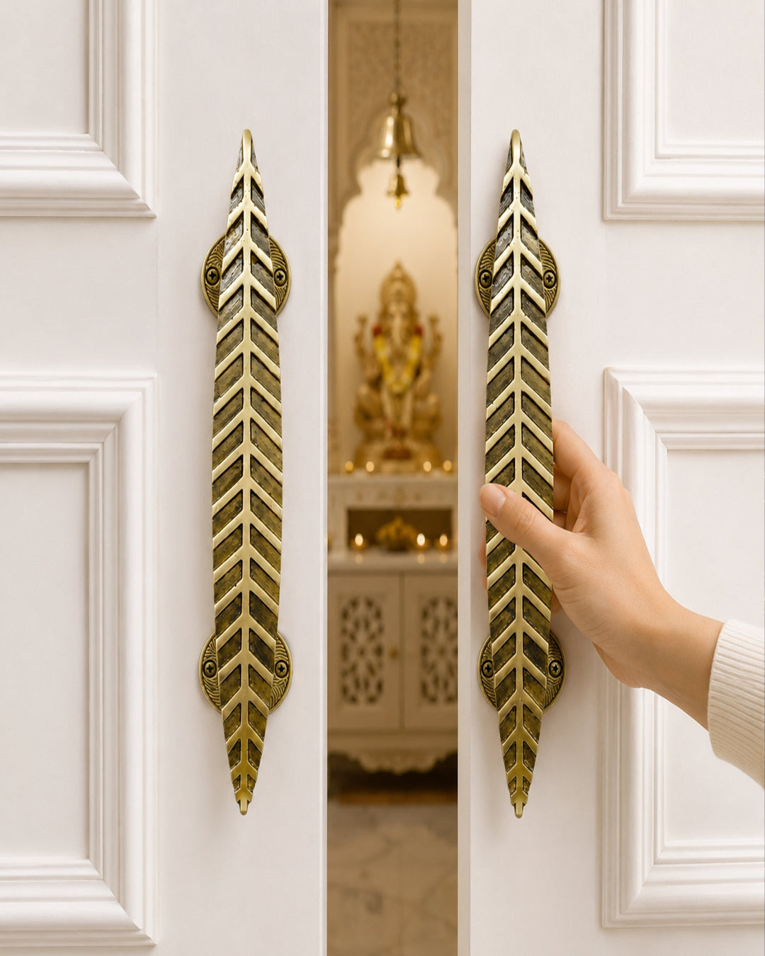 A hand is shown pulling a brass door handle on a white paneled door, with a matching handle visible on the other door. A warm interior with a decorative statue is visible behind the door.