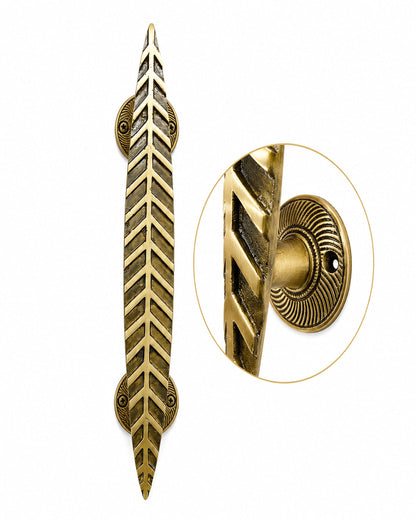 An ornate brass door pull handle with a leaf-like chevron pattern, shown alongside a circular close-up inset of its textured mounting plate.