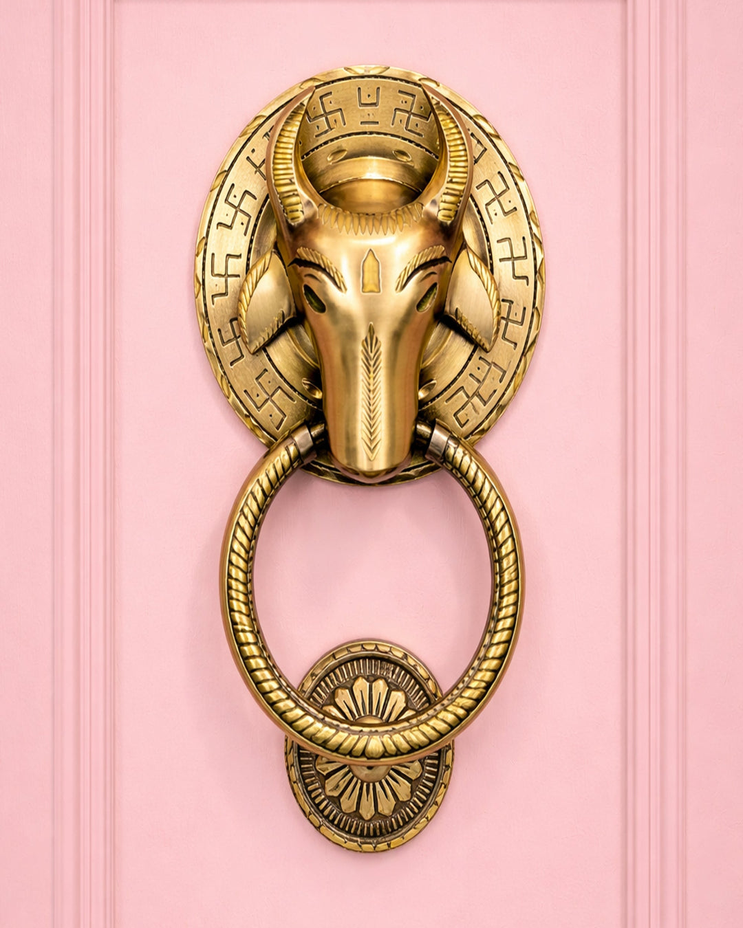 Decorative gold door knocker with ram's head design on a pink background
