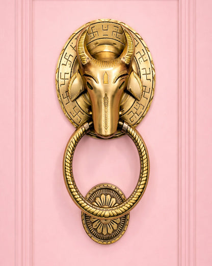 Decorative gold door knocker with ram's head design on a pink background