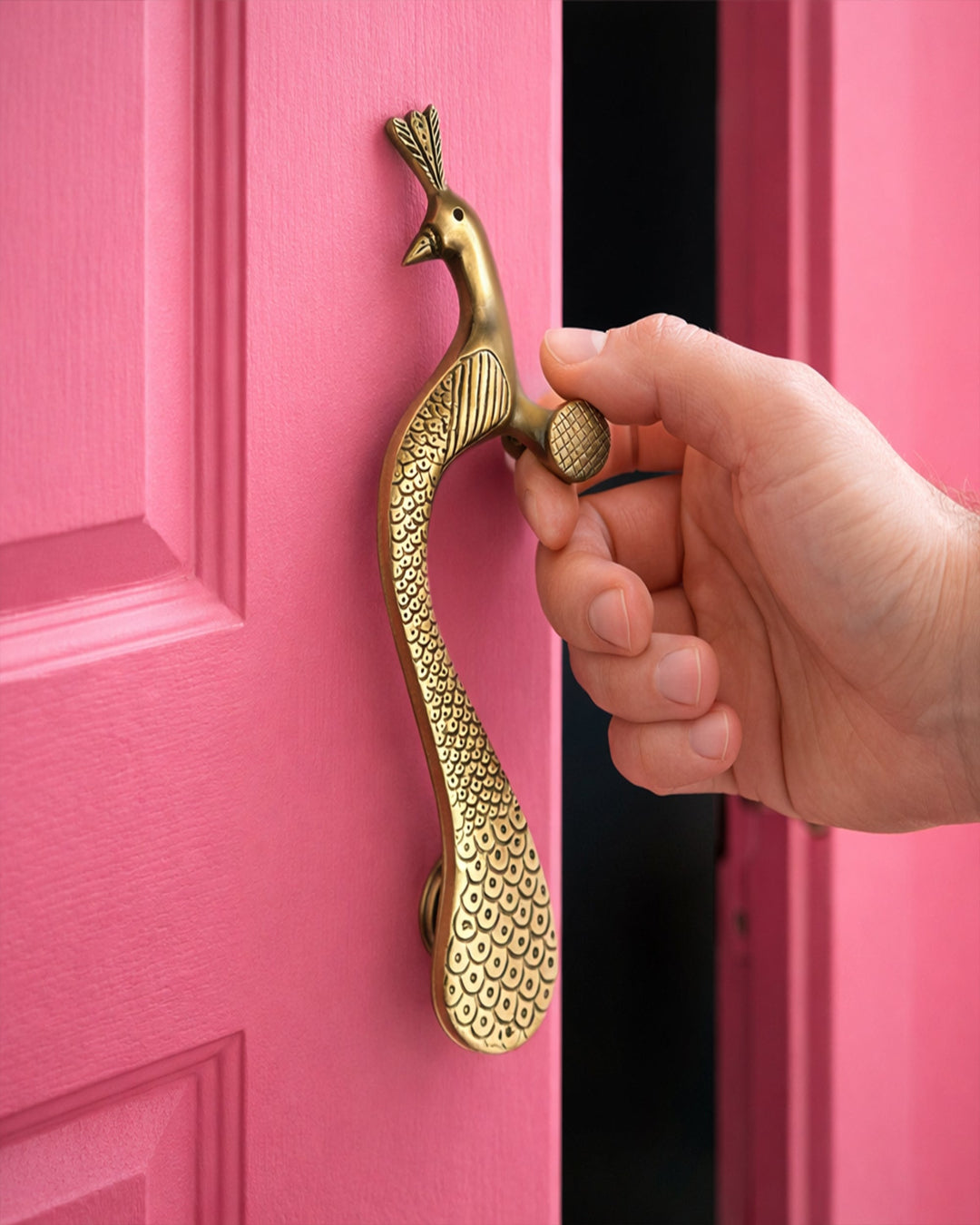 Hand opening a pink door with a decorative gold peacock handle.