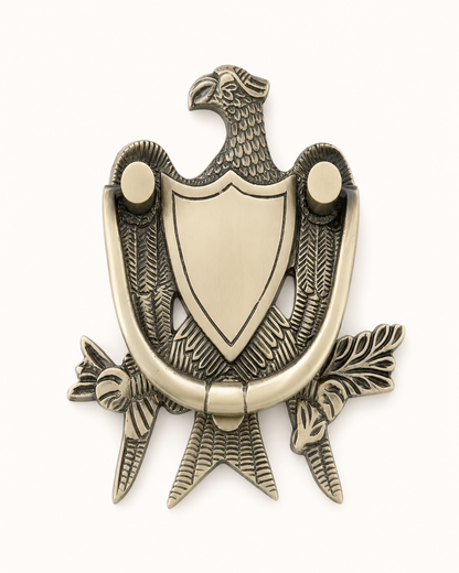 An antique bronze eagle door knocker with a central shield, detailed feathers, and a curved ring handle, shown on a plain white background.