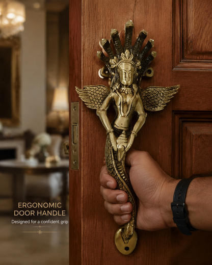 A hand holding a brass-finished ergonomic door handle shaped like a winged female figure with a serpent body, mounted on a wooden door. Text on the image reads 'ERGONOMIC DOOR HANDLE' and 'Designed for a confident grip.