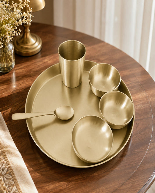 Set of gold tableware including plates, bowls, and a spoon on a wooden table.