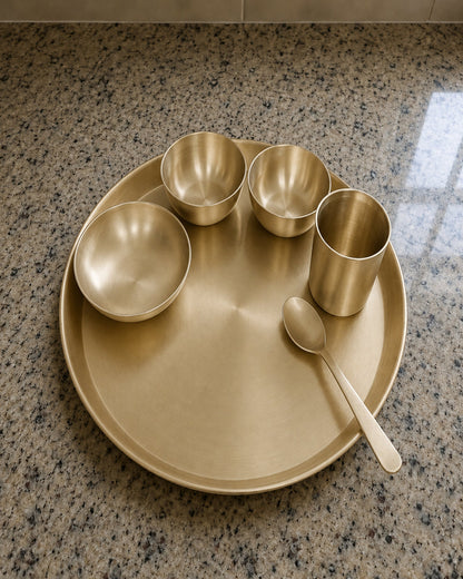 Set of gold ceramic dishes including bowls and a cup on a speckled countertop.