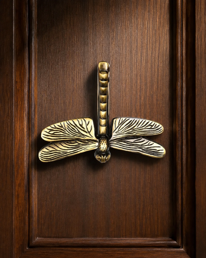 An ornate brass dragonfly door pull handle mounted on a dark brown wooden door.